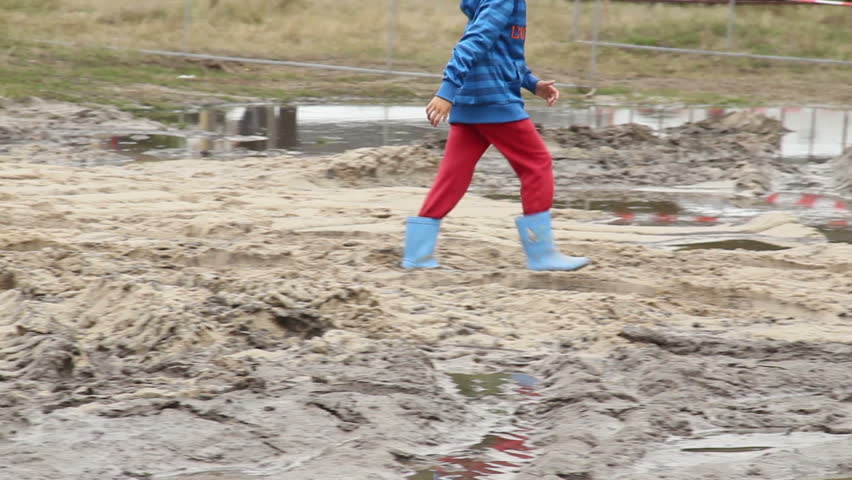 Child in boots walks on dirt puddle, children unsafety care