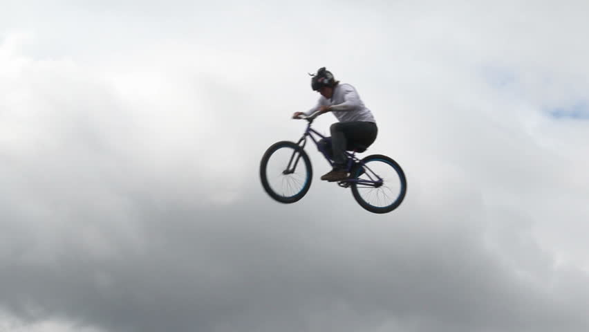 Man on bicycle jumps high in slow motion, cloudy background