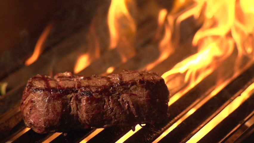Steak on grill with flames - slow motion shot