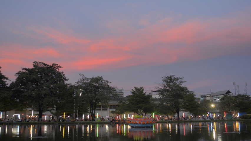 View across a pond of the Loi Krathong festival, with a colorful sky as the sun