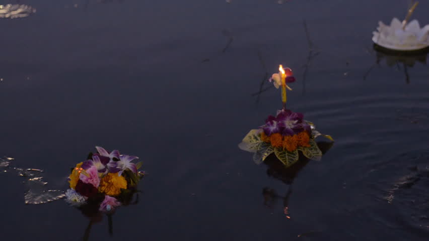 A small krathong made of flowers and banana leaves floating in a pond at dusk