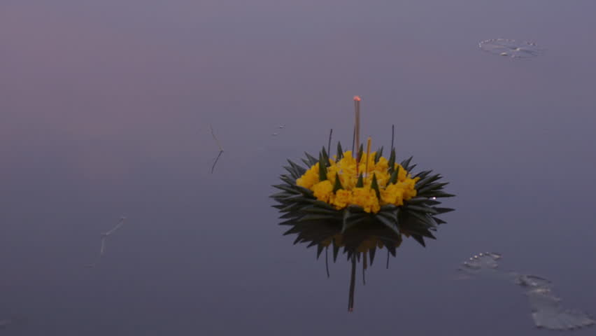 A krathong made of flowers and banana leaves floating by in a pond during the