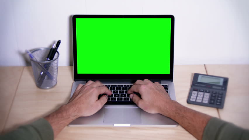 A man types on a laptop on his desk.  Green screen for your custom screen