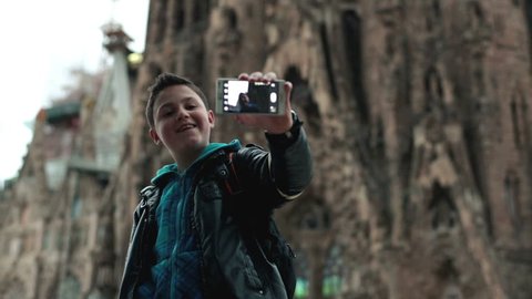 Boy taking picture of himself near cathedral Sagrada Familia with cellphone

