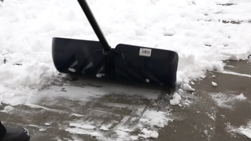 A woman shovels snow off of her driveway after a winter storm while her toddler