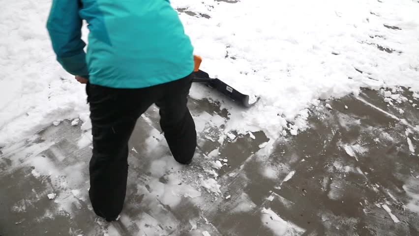 A woman shovels snow off of her driveway after a winter storm while her toddler