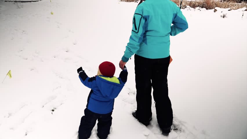 A mother and her baby boy playing outside in the snow after a large snowstorm.