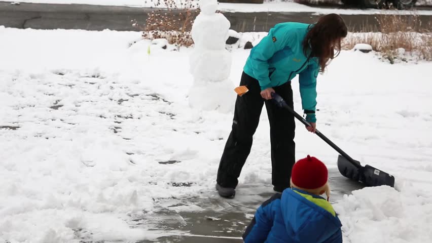 A mother and her baby boy shoveling snow off the driveway after a large