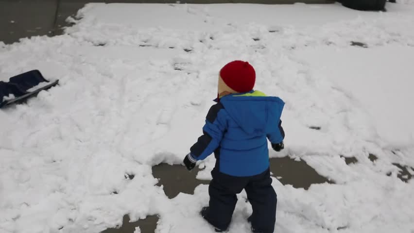 A mother and her baby boy playing outside in the snow after a large snowstorm.