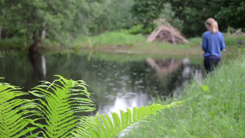 large green fern leaves in the background to the pond stands a girl with a fishing rod