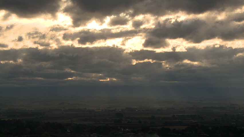 Sun breaks through storm clouds and shines light beams on the land below