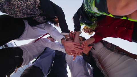 Motivational business team stand in a circle with their hands together for a team talk, outdoors in the city on a bright sunny day. In slow motion.