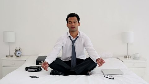 Happy handsome businessman meditating in bright bedroom