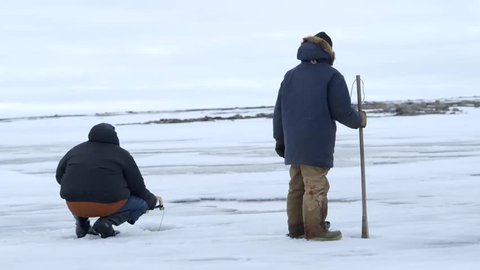 Pair of fisherman cut holes in sea ice during an Arctic expedition.