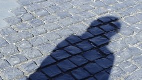 A woman's shadow is seen on the cobblestone pavement and is moving also. Can be used as a video metaphor, shadow  identity unknown, perception of identity, and movement = everyday life transformations