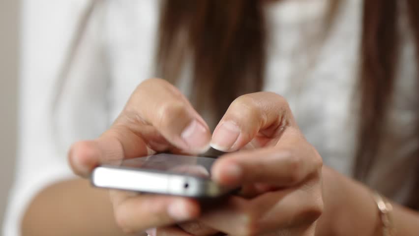Fingers of a young woman texting on a smartphone device.
