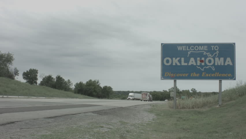 welcome to oklahoma sign with trucks and cars driving by on i-40.