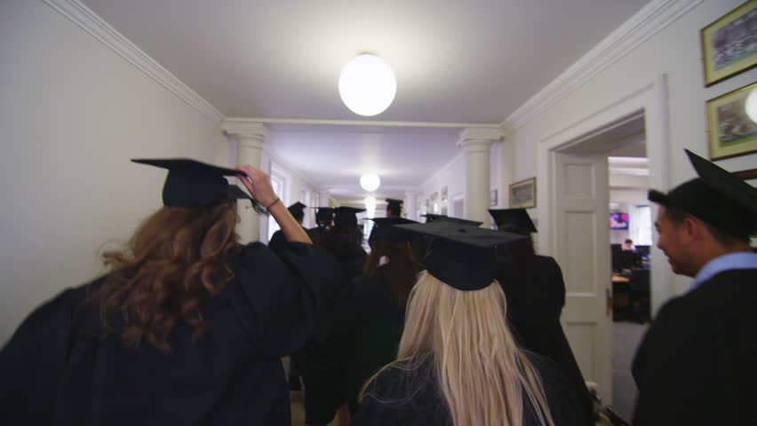 View from behind of excited mixed ethnicity group of university students on graduation day, running through the hallway of the university building dressed in caps and gowns. In slow motion.