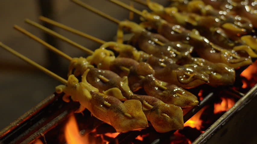 Skewers of squid being flame grilled by a street vendor in Bangkok, Thailand.