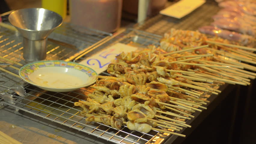 A Thai street food stall with skewers of grilled squid laid out ready for