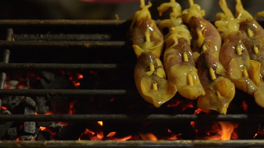 A Thai street food vendor laying out skewers of squid onto a grill in Bangkok,