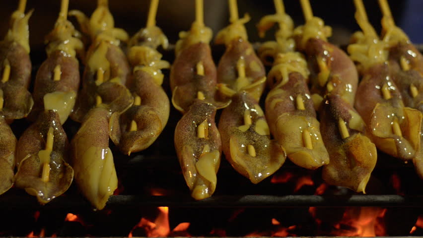 Skewers of fresh squid grilling at a street vendor's stall in Bangkok, Thailand.