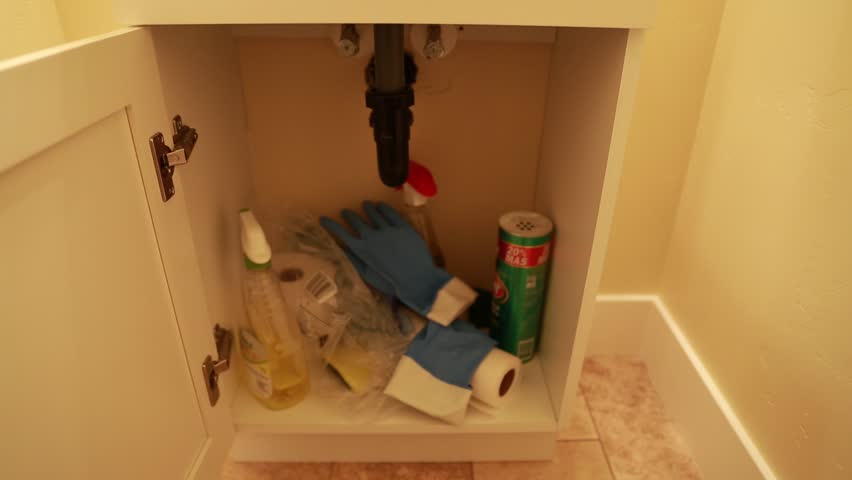 A hand opening a bathroom cupboard to look for cleaning supplies