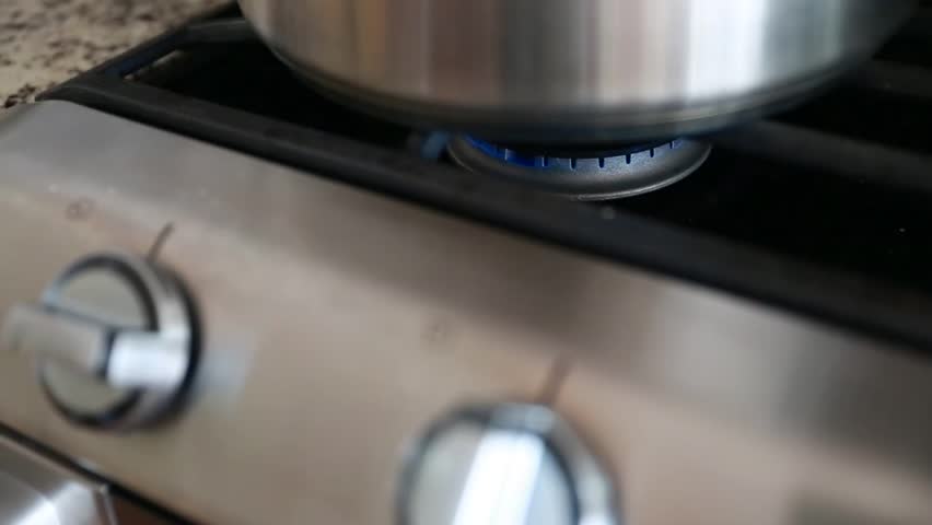 A stainless steel pot on a natural gas stovetop above the flame