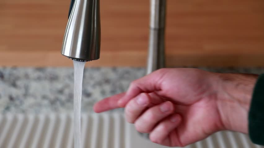 A man fills a glass of water from the kitchen sink