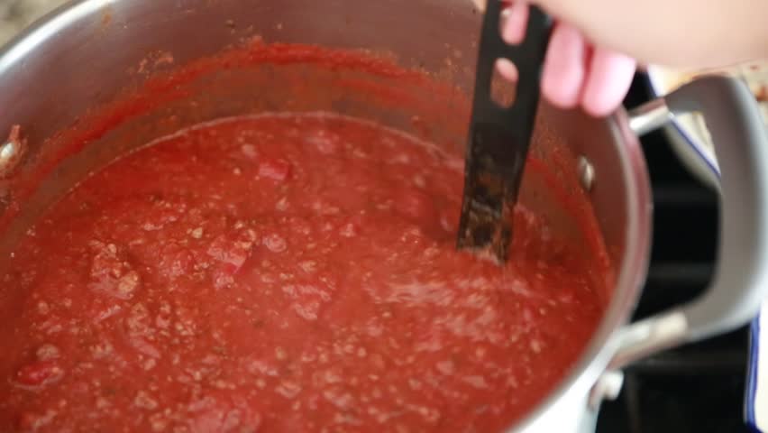a man stirs spaghetti sauce while in a pot on the stove