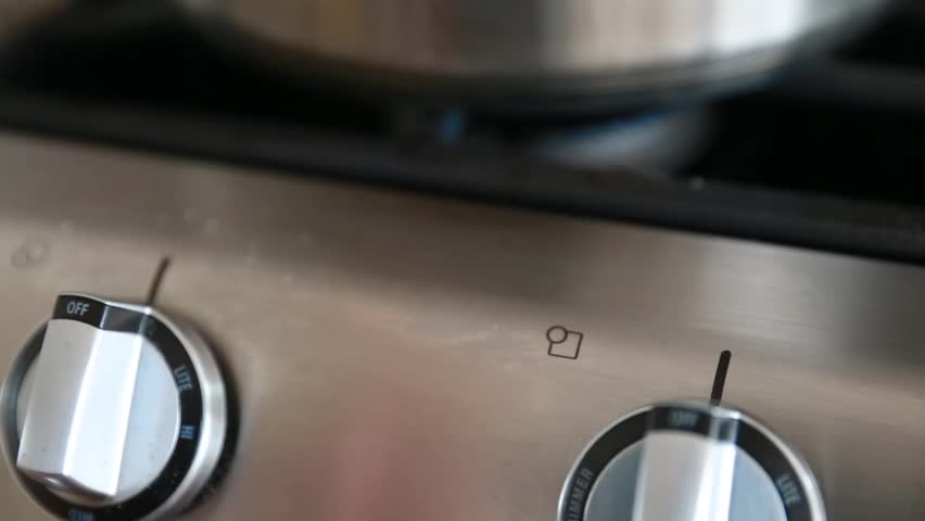 A stainless steel pot on a natural gas stovetop above the flame