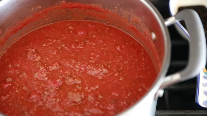 a man stirs spaghetti sauce while in a pot on the stove