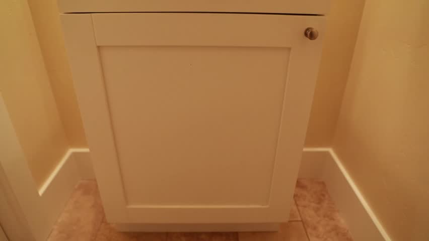 A hand opening a bathroom cupboard to look for cleaning chemicals