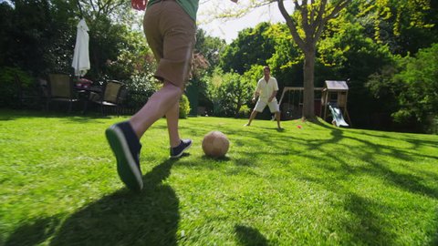 Active young boy playing soccer with his father outdoors on a bright sunny day. 