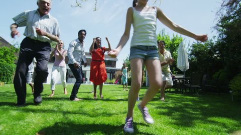 Happy mixed ethnicity group of friends and family with many generations, playing sports and having fun in the garden on a summer day. In slow motion.