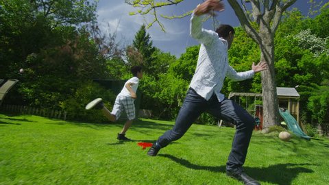 Cute young asian boy playing soccer with his father in the garden on a bright summer day. In slow motion.