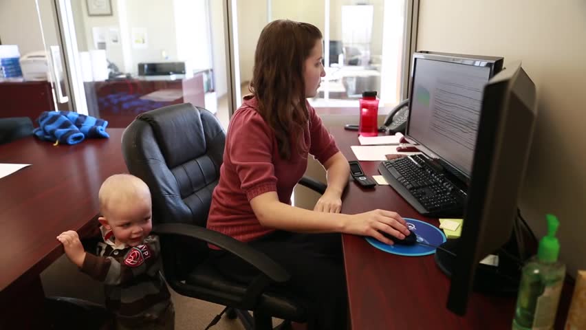 A mother working in the office with her little toddler boy by her side