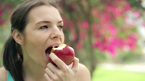Portrait of young woman eating red apple, sitting in park
