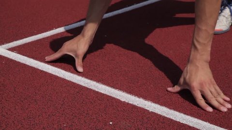 An athlete, a runner, puts his hand down on a red track of an olympic stadium