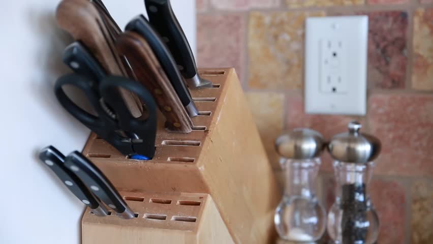 A man pulls a knife from a knife block in the kitchen