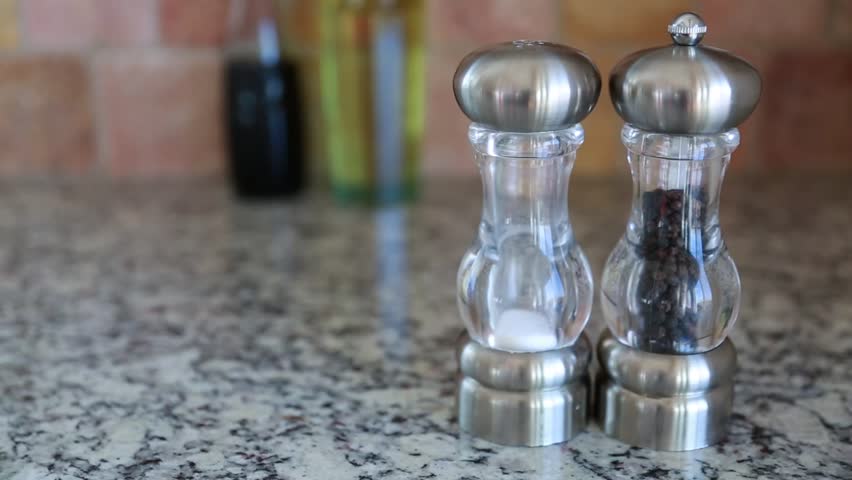 A hand grabs salt and pepper shakers off the kitchen counter