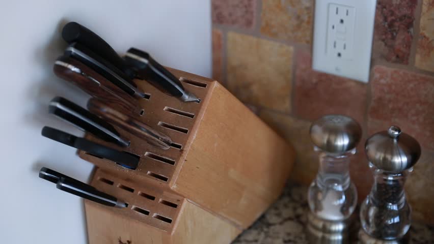 A man uses knifes from a knife block in a kitchen