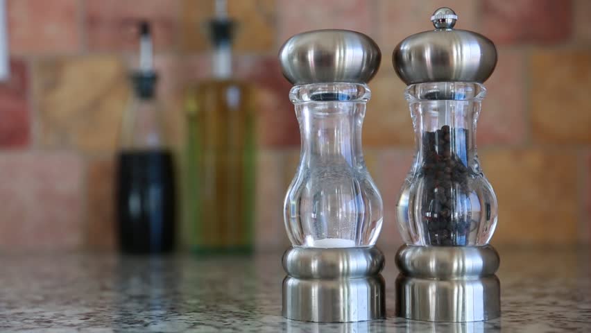 A hand grabs the salt and pepper shakers off of a kitchen granite countertop