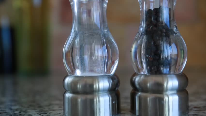 A hand grabs the salt and pepper shakers off of a kitchen granite countertop
