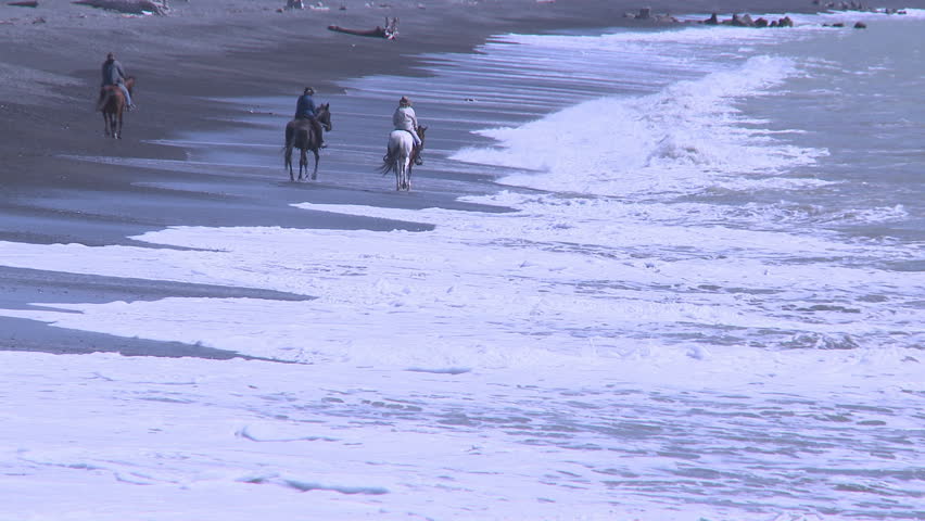 Horses and riders in the surf as they travel along a deserted beach