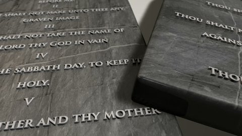 A slow close up pan across two stone tablets with the ten commandments inscribed onto them on an isolated background