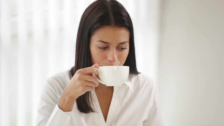 Beautiful young woman sitting at office desk using laptop drinking tea looking