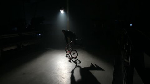 BMX rider doing tricks in dark warehouse Stock Video