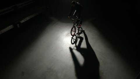BMX rider doing tricks in dark warehouse Stock Video