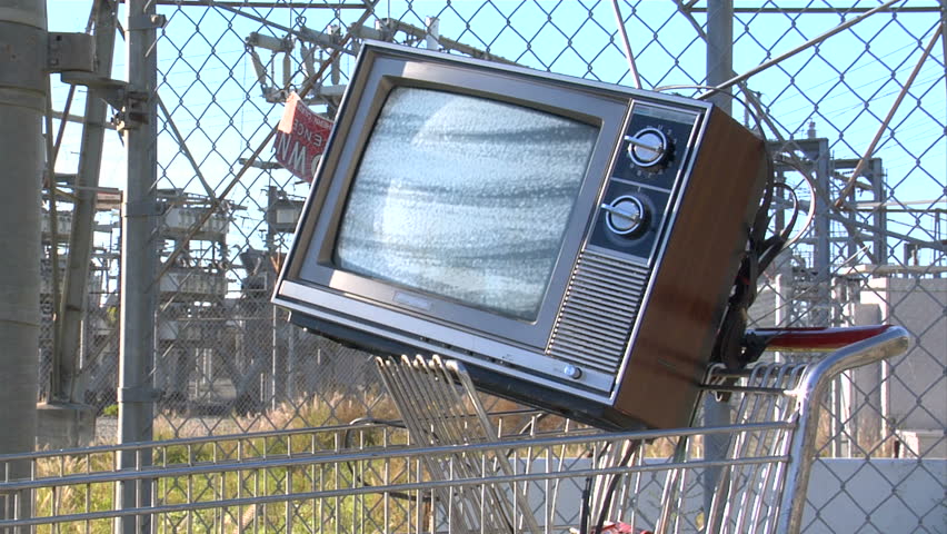 This is a unique shot of a retro tv in a shopping cart in front of a power